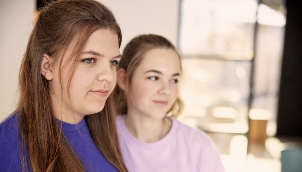 Nora ist von der Seite abgebildet und blickt in die Ferne, im Hintergrund ist ihre Schwester zu sehen.