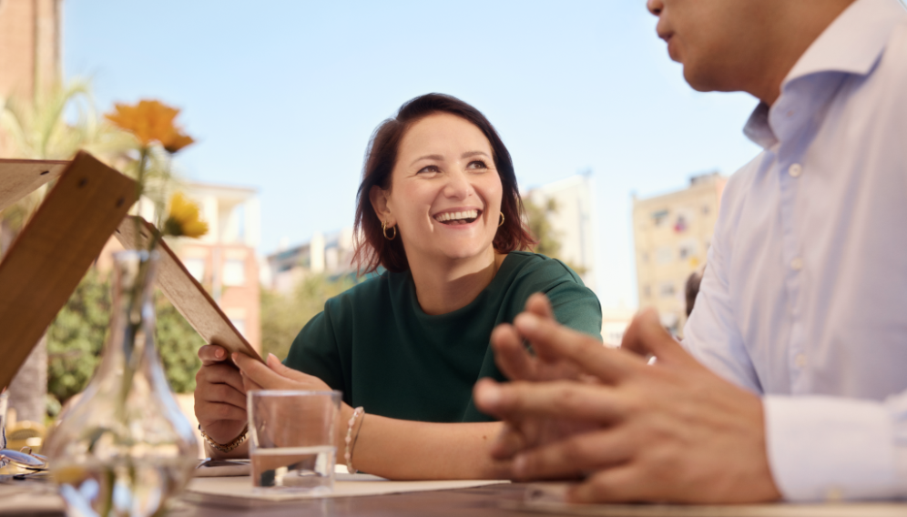 Veerle lacht, während sie mit ihren Freunden an einem Restauranttisch plaudert.