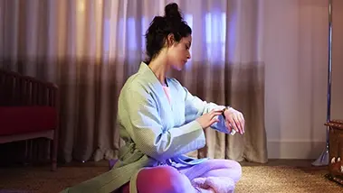 Eine Frau sitzt auf dem Boden und macht Yoga, schaut auf die Uhr an ihrem Handgelenk.