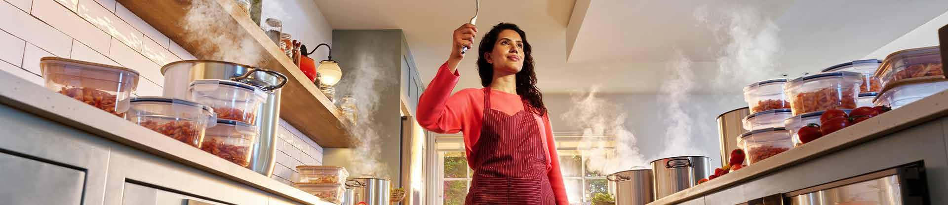 Woman standing in a kitchen preparing food with organised meal containers on the counter.